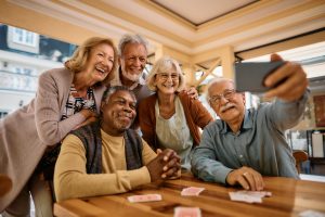 Multiracial group of happy senior people taking selfie with cell phone in nursing home.